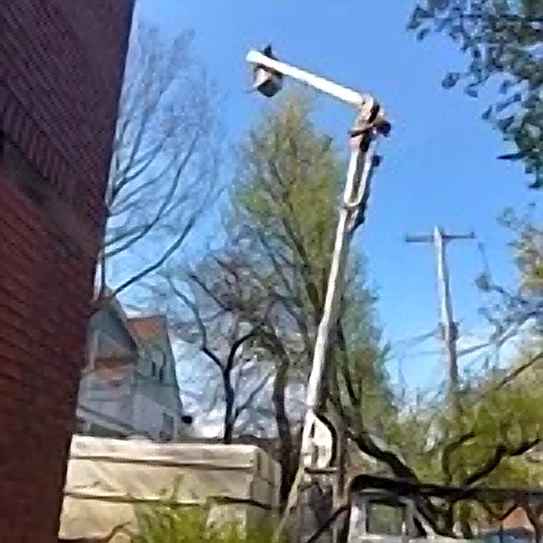 Kenwood Tree Service bucket lift raised beside a brick building